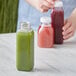 A woman pouring green juice into a customizable square PET clear bottle.
