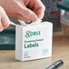 A hand opening a white box of Noble Products dissolving product labels.