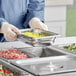 A person in a blue uniform using a Vollrath stainless steel tray to prepare food on a counter.