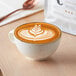 A cup of Arrosto decaf coffee with a leaf design in the foam sits on a table.