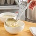 A person using a Choice stainless steel ladle to pour soup into a bowl.