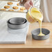 A woman pouring yellow cake batter into a Baker's Mark round cake pan.