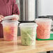 A woman holding a Choice translucent plastic food storage container filled with green beans.