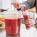 A person using a Choice condiment pump to pour red liquid into a large plastic container.