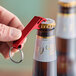 A hand holding a Franmara red aluminum bottle opener with key ring.