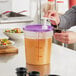 A woman using a Choice condiment pump to pour liquid into a translucent container with a purple lid.