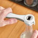 A person using a Franmara gray multi-purpose bottle opener to open a bottle.