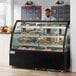 A man in a blue shirt standing behind an Avantco dry bakery display case with pastries on it.