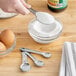 A person using a Choice stainless steel measuring spoon to measure sugar over a bowl.