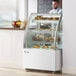 A man standing behind a white Avantco dry bakery display case filled with pastries.