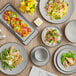 A table with Acopa Apollo matte grey and black coupe plates of food.