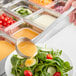 A person using a Choice stainless steel ladle to pour sauce over a bowl of salad.