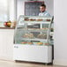 A man standing behind a white Avantco dry bakery display case filled with pastries.