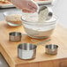 A person using Choice stainless steel measuring cups to measure flour into a bowl.