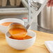 A person using a Choice stainless steel ladle to pour soup into a bowl.