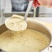 A person holding a Choice stainless steel ladle over a pot of soup.