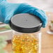 A gloved hand holding a black 89/400 plastic cap with foam liner over a jar of yellow pills.