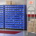 A Regency wire shelving unit with blue storage bins in a large warehouse.
