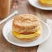 An English muffin breakfast sandwich with sausage, eggs, and cheese on a plate.