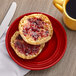 A Tuxton Concentrix cayenne China plate with a muffin and jam on it and a yellow mug of coffee.