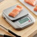 A stainless steel digital kitchen scale with a piece of raw salmon on the platform.