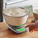 A digital kitchen scale with a large glass bowl filled with flour on top.