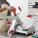 A man using a Berkel medium-duty meat slicer to slice a tomato.