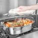 A person holding a towel over a Vollrath Miramar French oven full of meat and vegetables.