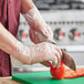 A person in a chef's uniform cutting a tomato with Noble NexGen disposable gloves.