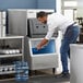 A man in a white shirt pouring water into a Hoshizaki ice storage bin.