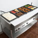 A black Cambro high heat plastic food pan on a table with trays of food.