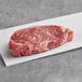 A piece of Rastelli's raw Black Angus New York Strip Steak on a white surface.