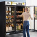 A woman opening an Avantco wine merchandiser with bottles of wine on shelves.