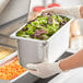 A person in gloves holding a Vollrath stainless steel hotel pan of salad on a counter.