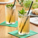 Two glasses of Tractor Beverage Co. green tea with black straws and leaves on a table.
