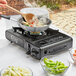 A person cooking food on a Choice portable butane stove.