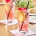 Two glasses of Tractor Beverage Co. Organic Hibiscus drink with pink straws on a table.