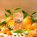 A glass of Tractor Beverage Co. Organic Mandarin & Cardamom juice concentrate with oranges and green leaves.