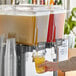 A person pouring Tractor Beverage Co. Organic Green Tea concentrate into a drink dispenser.