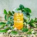 A glass jar with ice and Tractor Beverage Co. Organic Green Tea Beverage on a white background surrounded by leaves.