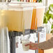 A person pouring Tractor Beverage Co. Organic Lemonade into a juice dispenser.