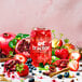 A glass of Tractor Beverage Co. Organic Berry Patch juice concentrate with red liquid and a straw, surrounded by a variety of berries.