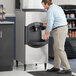 A man holding a bucket of ice next to an Avantco ice machine.