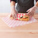 A person wearing gloves wrapping a sandwich in red check deli paper.