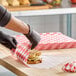 A sheet of red check deli sandwich wrap paper being used to wrap a sandwich on a wooden counter.
