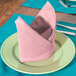 A folded pink Intedge cloth napkin on a plate with silverware.