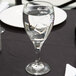 A Libbey Teardrop goblet filled with ice water on a table with a plate and silverware.