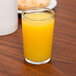 A Libbey juice glass filled with orange juice on a table.