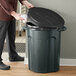 A man cleaning a Toter trash can with a black lid.