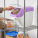 A person pouring rice into a white and purple Baker's Lane ingredient bin.